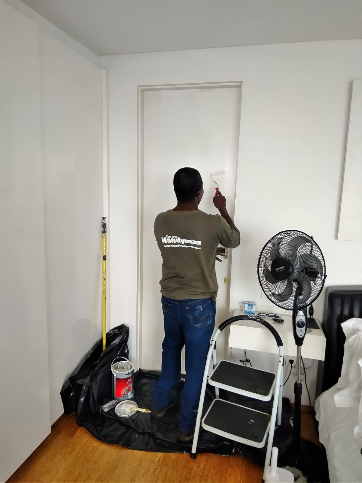 Bruce in a Bruce Handyman shirt rolling paint onto a door